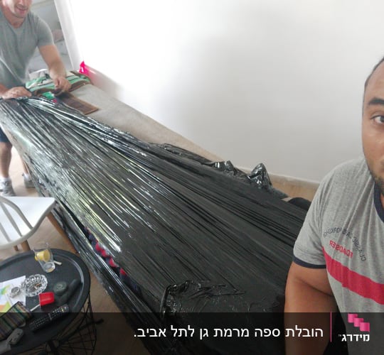 שני אנשים עוטפים רהיט בניילון שחור למעבר דירה